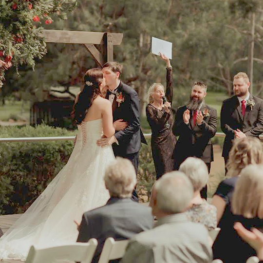 Sue celebrating while the newly married couple kiss